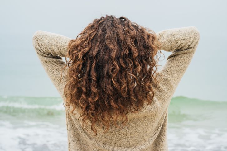 Woman with brown wavy hair facing the ocean Woman with brown wavy hair facing the ocean
