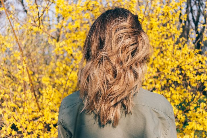 Blond woman facing forsythia bush Blond woman facing forsythia bush