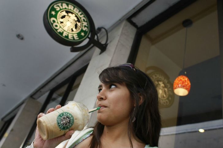 A woman sips from a straw outside of a Starbucks location