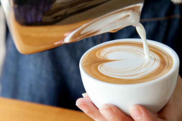 Milk is poured over a cup of coffee in a decorative pattern