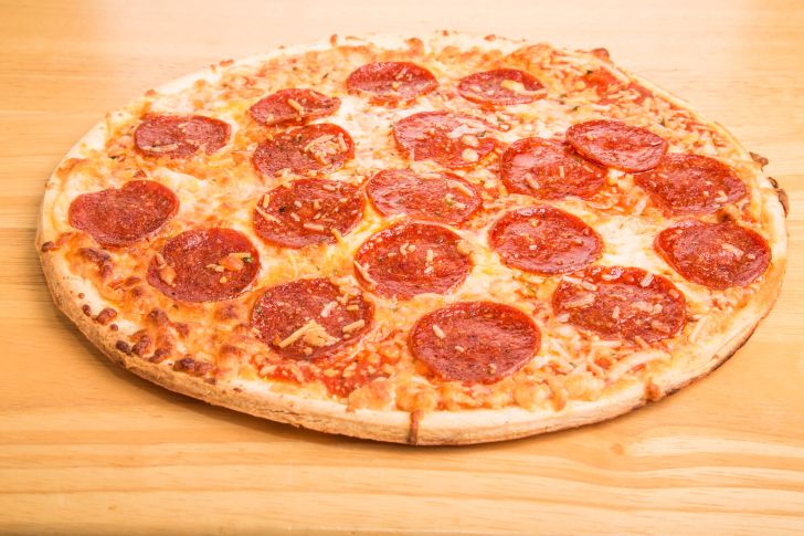 Whole pepperoni pizza on wood cutting board
