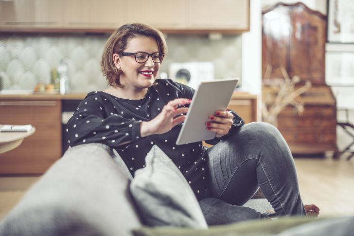 A smiling woman seated on a couch using a tablet