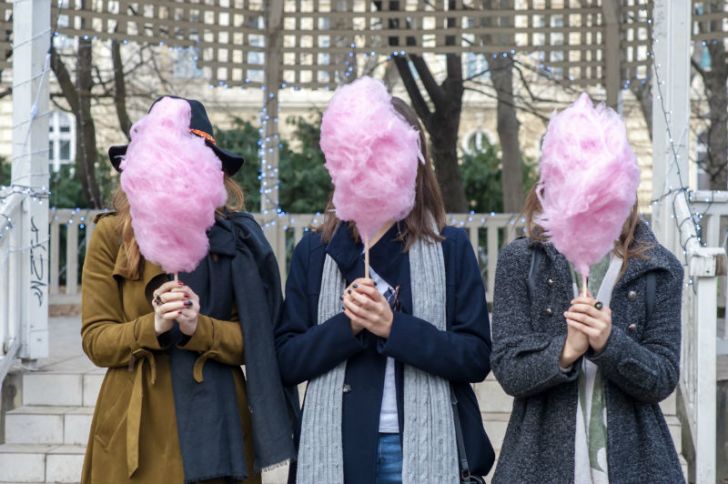 Three people hold up cotton candy in front of their faces