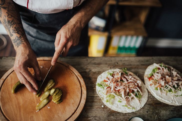 A chef slicing pickles to put into a wrap or taco