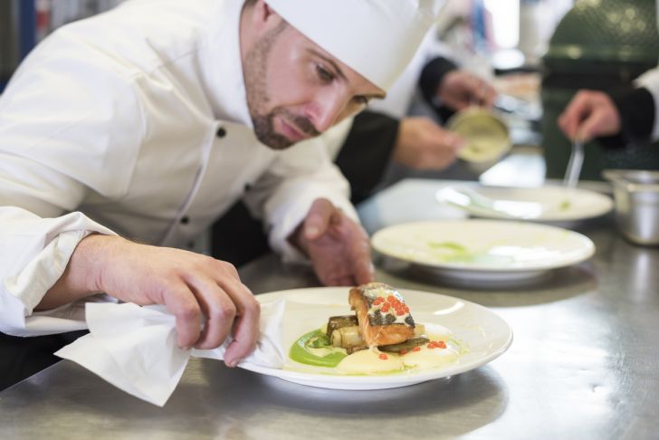 A chef staring intently at a dish of salmon