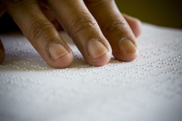 A person reads a page of Braille by running their fingers over it