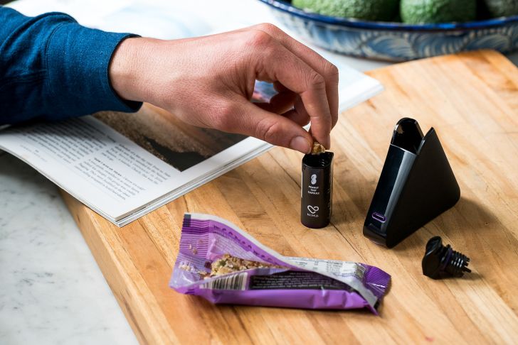A hand loads a piece of an energy bar into a Nima peanut sensor capsule.