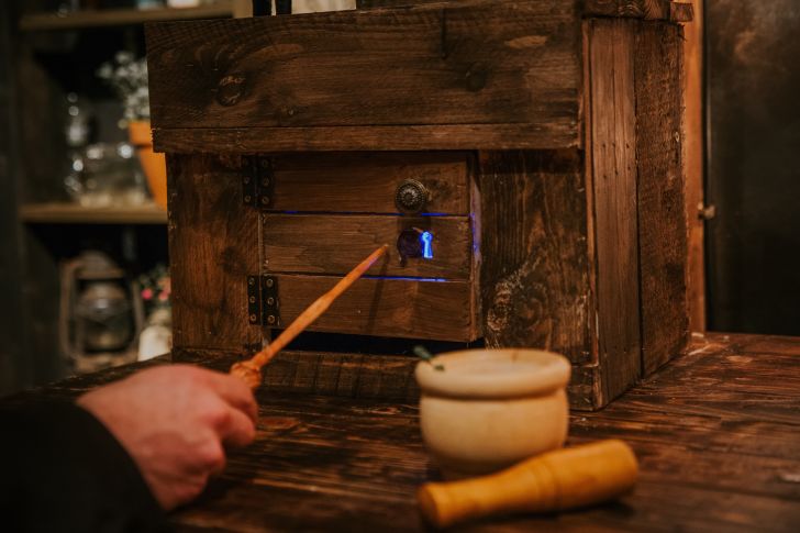 A person taps a wand on a wooden box in a mixology class.