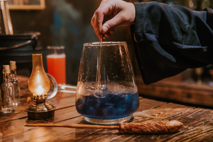 A person in a robe stirs a blue cocktail.