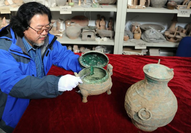 An archaeologist holds a bronze vessel where soup was found inside