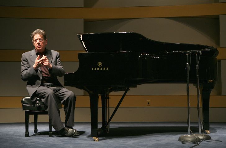 Composer Philip Glass sitting at a grand piano.