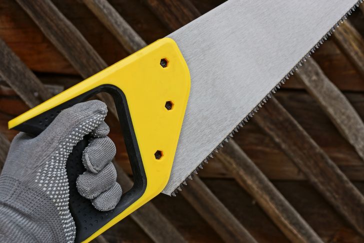 A gloved hand holding a handsaw