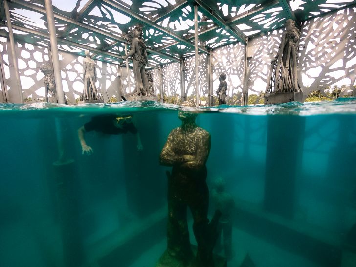 A snorkeler looks at a partially submerged sculpture