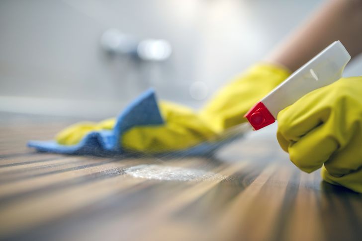 A person cleaning a table top with spray and a cloth.
