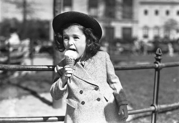 black and white photo of a young well-dressed girl eating an ice cream cone