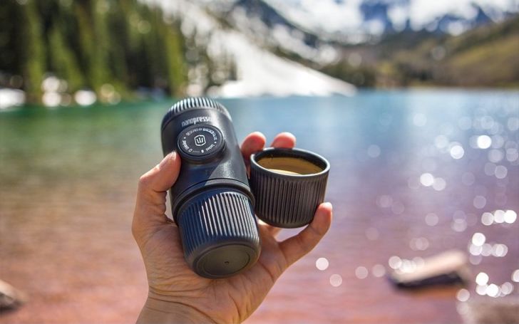 Hand holding a tiny espresso machine by a lake.