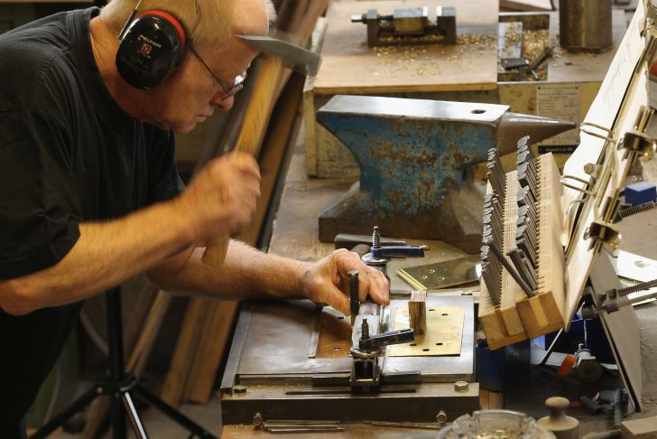A man in a shop holding a hammer making a Stolpersteine.