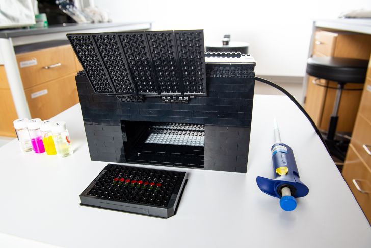 An open black LEGO box sits in the lab in front of a chemical test plate.