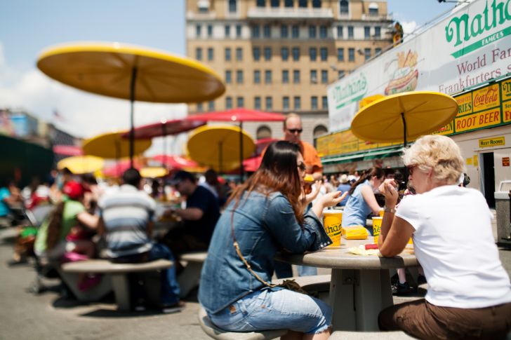Image of people sitting under umbrellas at the original Nathan's Famous location
