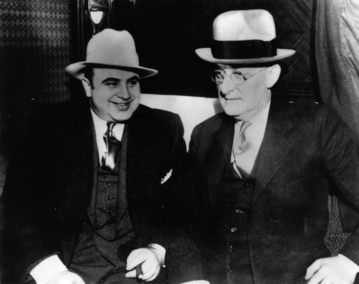 Vintage photograph of Al Capone standing next to some other unknown nameless guy in a fedora. Or maybe a bowler hat.
