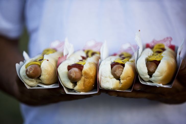 Image of a man in a white shirt holding four hot dogs