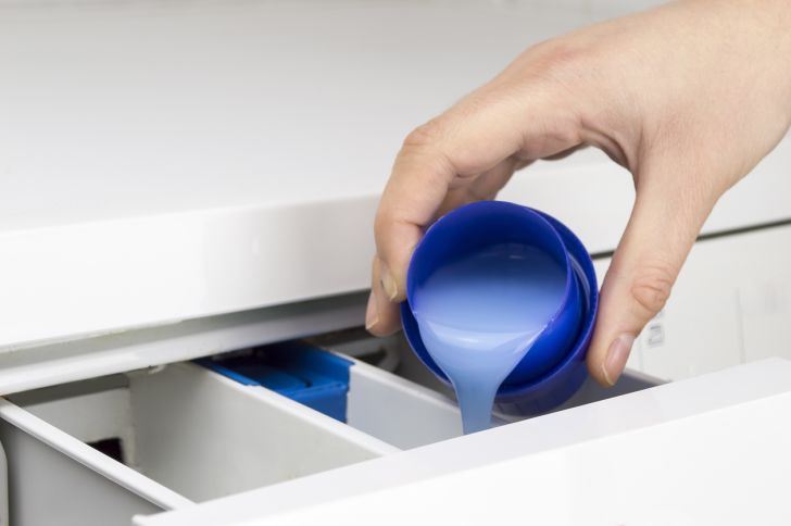A hand adding soap to a washing machine