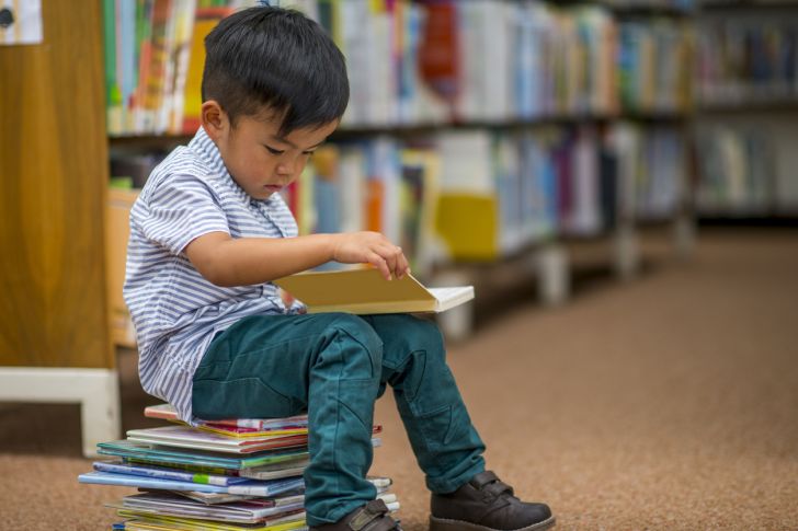 Little boy sitting on a stack of books and reading