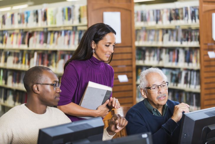 A librarian helping two patrons at computers