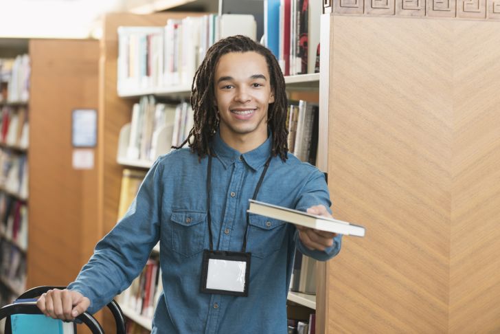 A young man handing over a book at a library
