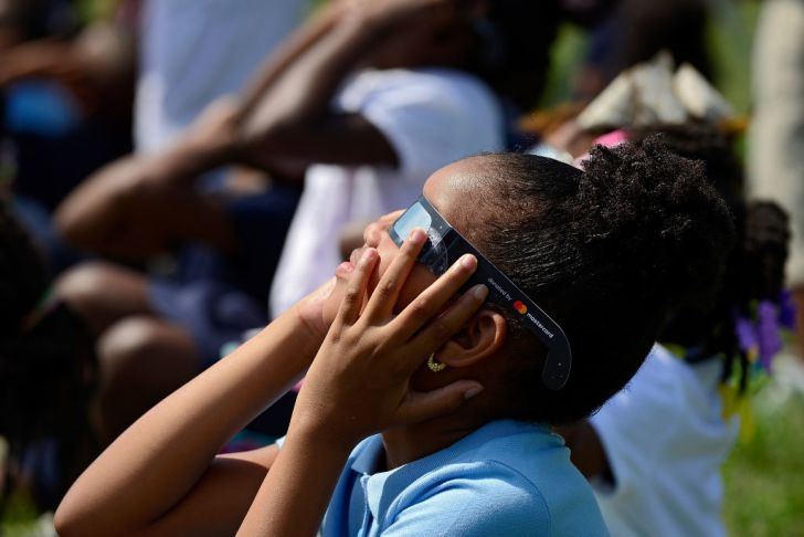 girl in eclipse glasses looks up at the sun