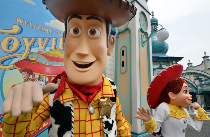 A costumed character that of Woody from Toy Story smiles at the camera while a costumed Jessie stands in the background.