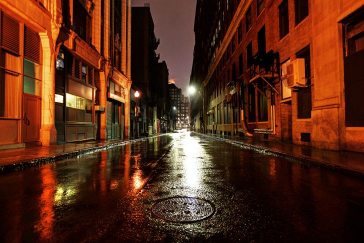 A wet street is photographed at night