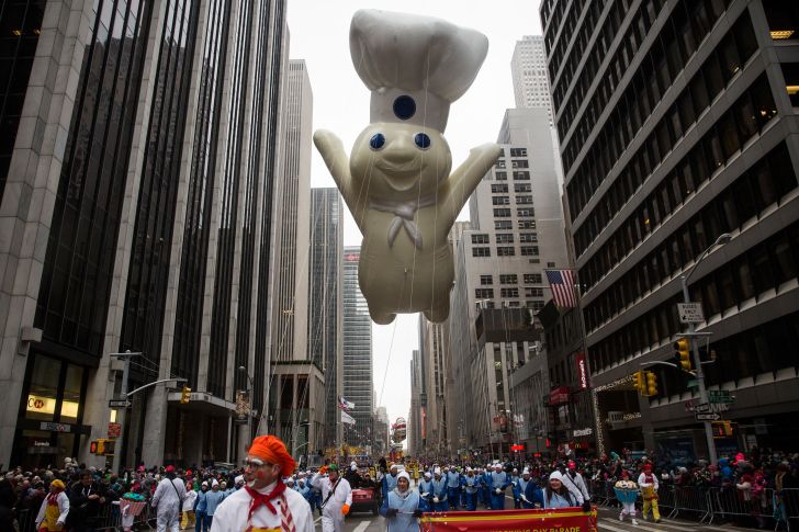 The Pillsbury Doughboy balloon floating down the street between skyscrapers at the Macy's Thanksgiving Day parade.
