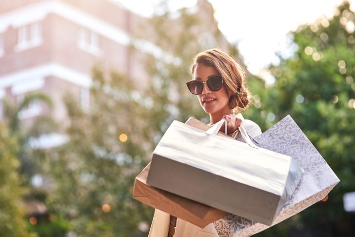 A woman in sunglasses carrying multiple pastel shopping bags