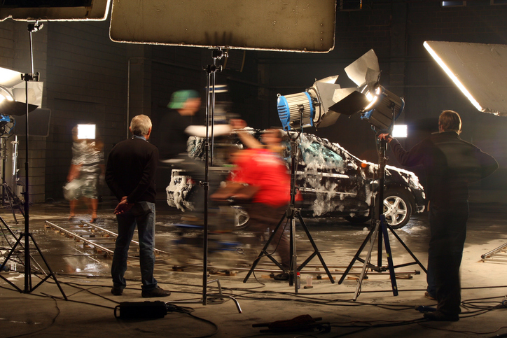 Members of a film crew standing near a car covered in water or soap under lights.