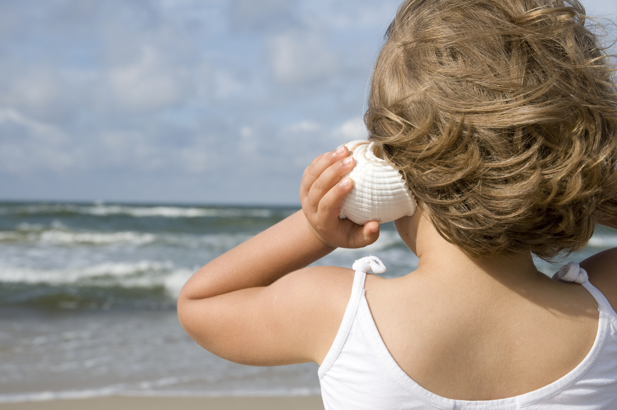 A child holds a seashell up to her ear